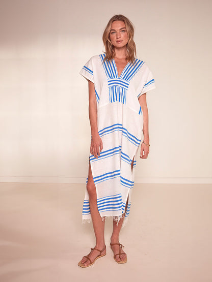 Woman Standing Wearing lemlem Gasira V Neck Caftan Featuring crisp white background and bright blue stripes and dots pattern