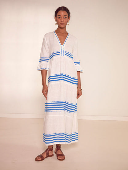 Woman Standing Wearing  lemlem Hawi Flutter Dress Featuring crisp white background and bright blue stripes and dots pattern