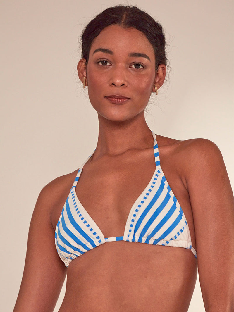 Close up of a Woman Standing Wearing lemlem malia string triangle top Featuring crisp white background and bright blue stripes and dots pattern and a matching string bikini bottom