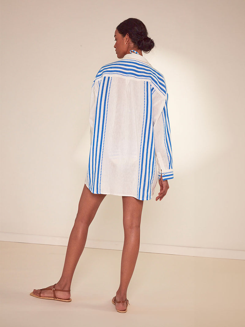 Back View of a Woman Standing lemlem Mariam Shirt Featuring crisp white background and bright blue stripes and dots pattern, matching tirangle top and bikini bottom
