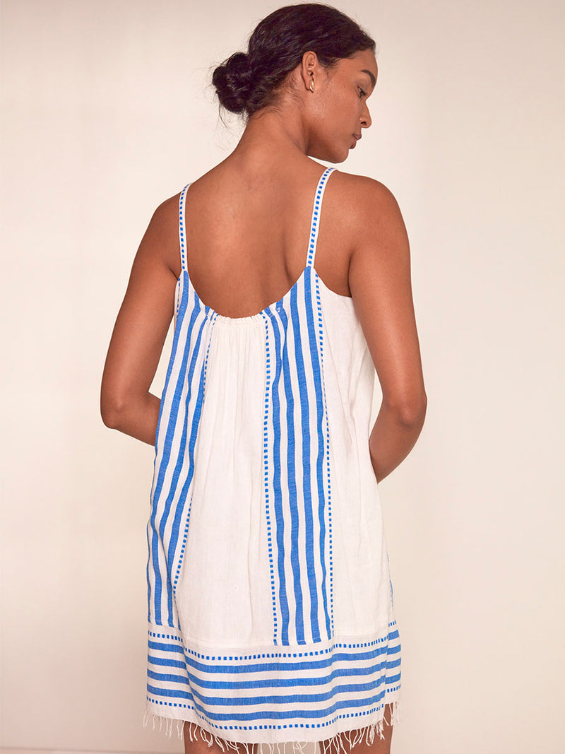 Back View of a Woman Standing Wearing lemlem Zina Swing Dress Featuring crisp white background and bright blue stripes and dots pattern