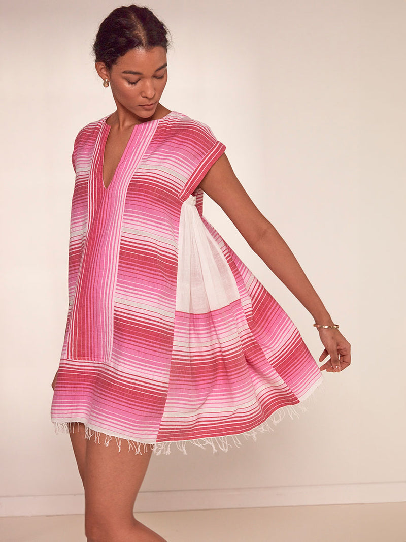 Side Shot of a Woman Standing Wearing emlem Elina Caftan Dress featuring white, soft pink, and raspberry stripes that effortlessly blend into a stunning ombre effect