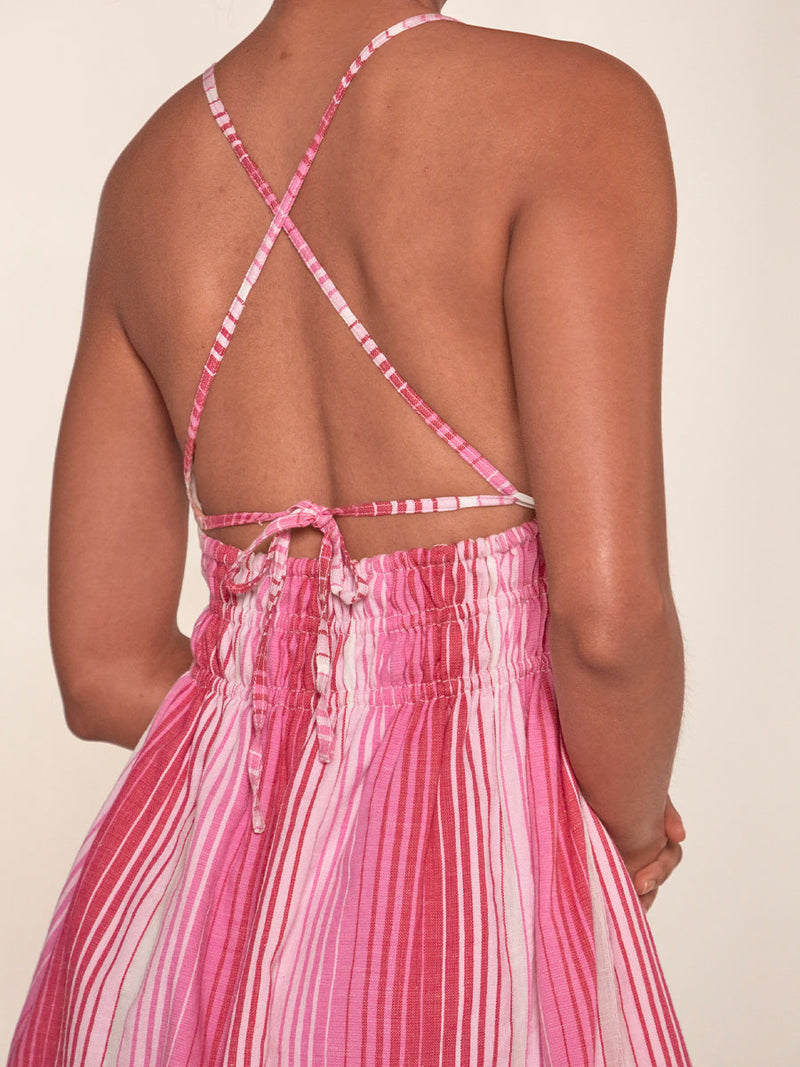 Close up on a back of a Woman Standing Wearing lemlem Kayla Short Triangle Dress featuring white, soft pink, and raspberry stripes that effortlessly blend into a stunning ombre effect