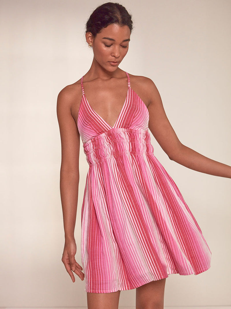 Woman Standing Wearing lemlem Kayla Short Triangle Dress featuring white, soft pink, and raspberry stripes that effortlessly blend into a stunning ombre effect