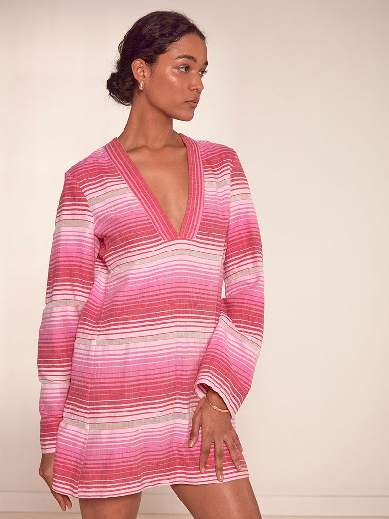 Woman Standing Wearing lemlem Raey Dress featuring white, soft pink, and raspberry stripes that effortlessly blend into a stunning ombre effect