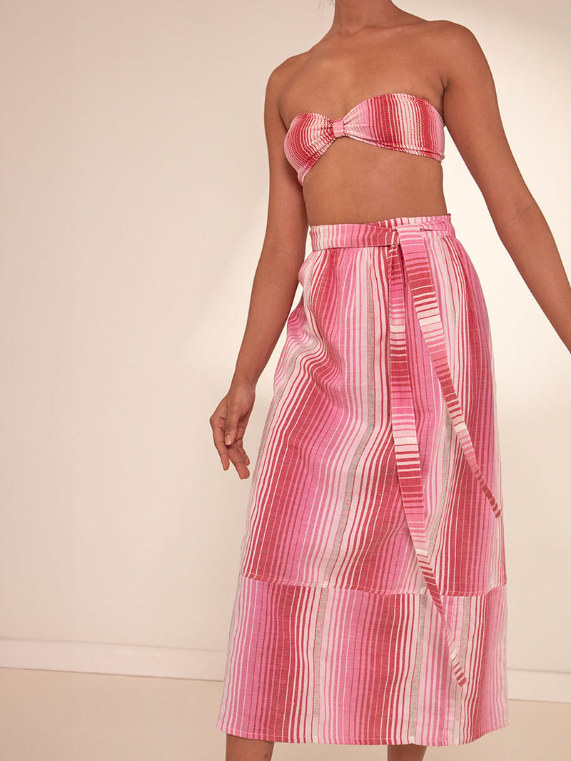 Close up  Shot of a Woman Standing Wearing lemlem Salana Wrap Skirt featuring white, soft pink, and raspberry stripes that effortlessly blend into a stunning ombre effect