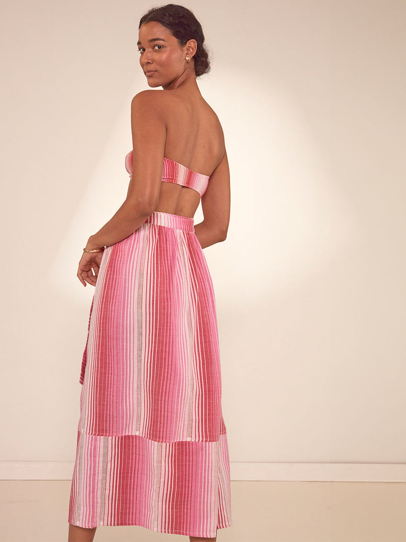 Back Shot of a Woman Standing Wearing lemlem Salana Wrap Skirt featuring white, soft pink, and raspberry stripes that effortlessly blend into a stunning ombre effect