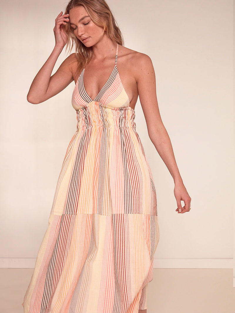 Woman Standing Wearing lemlem Gete Triangle Dress Featuring continuous stripe pattern in warm yellow, orange and peach tones.