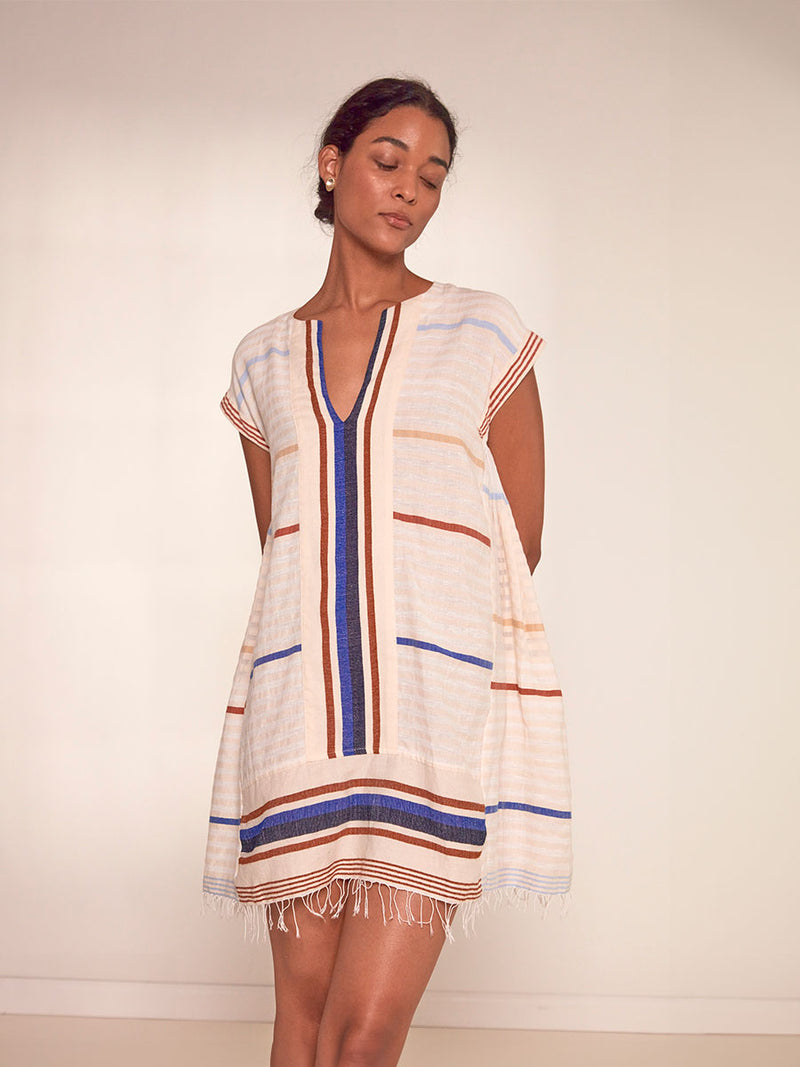 Woman Standing Wearing  lemlem Elina Caftan featuring striking bold stripe design in blue and brown hues on a neutral background