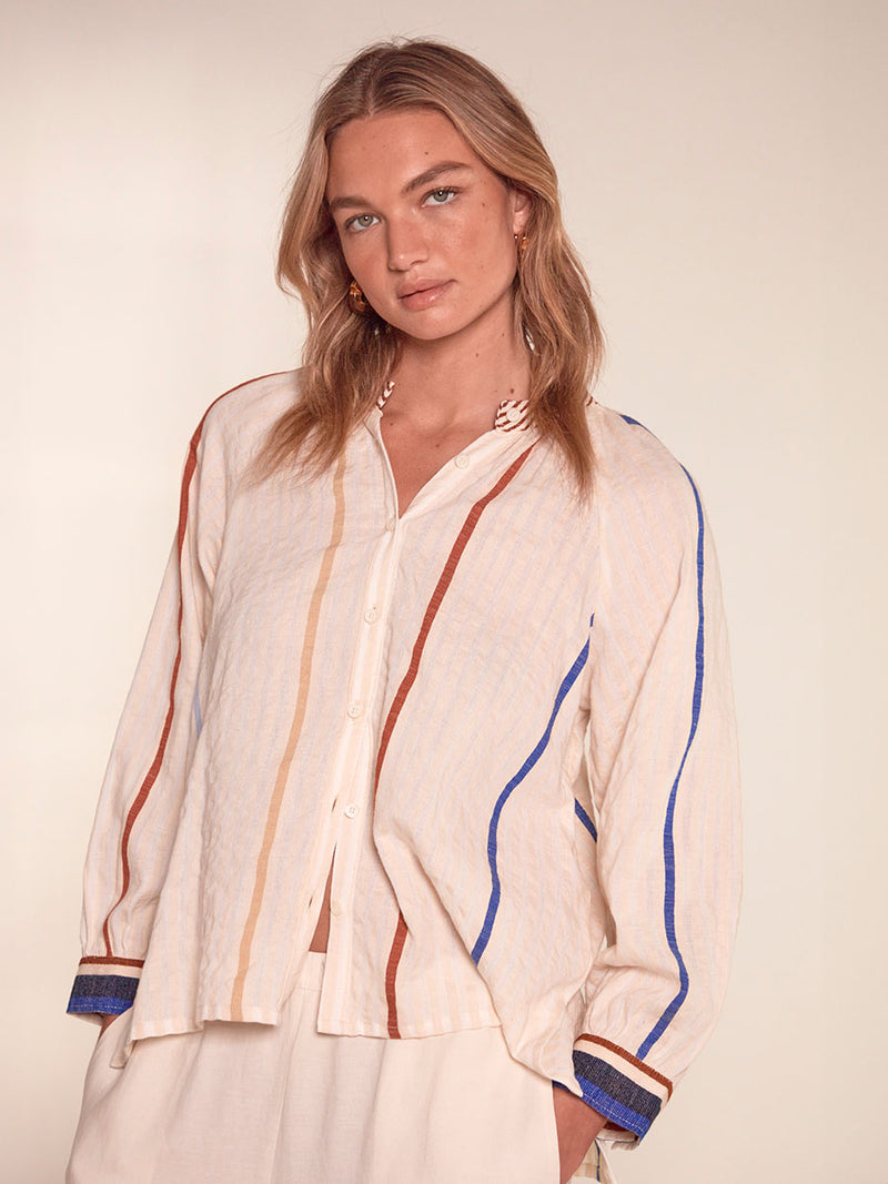 Woman Standing Wearing Mita Button Up Blouse featuring striking bold stripe design in blue and brown hues on a neutral background