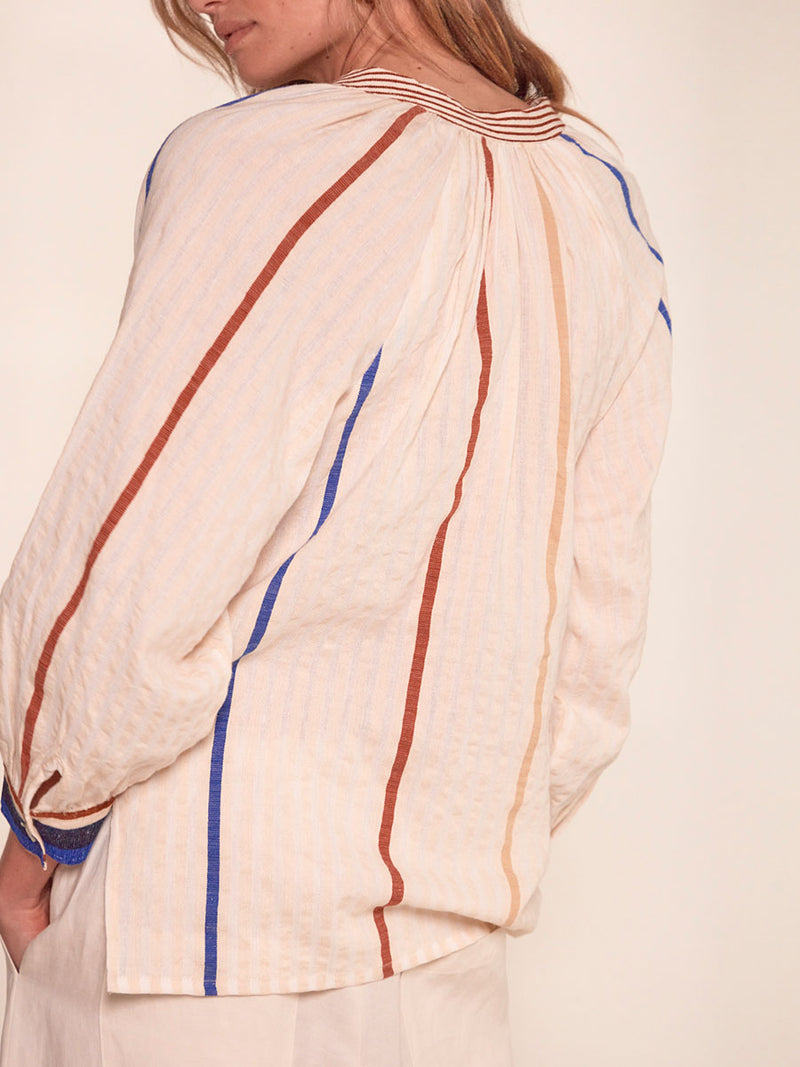Back of a Woman Standing Wearing Mita Button Up Blouse featuring striking bold stripe design in blue and brown hues on a neutral background