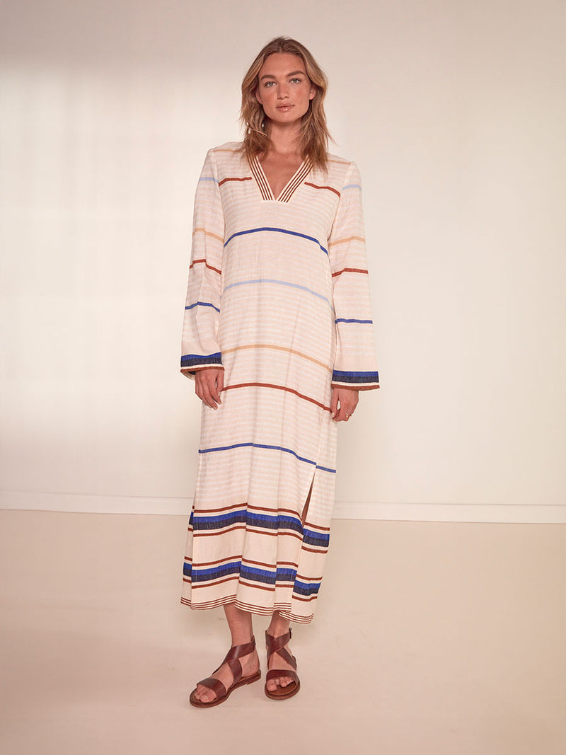  Woman Standing Wearing lemlem Theodora Column Dress featuring striking bold stripe design in blue and brown hues on a neutral background