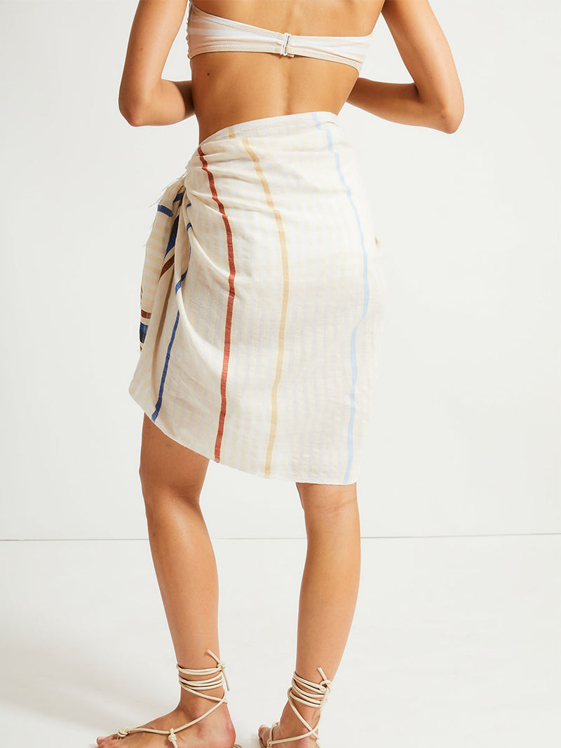 Back of a  Woman Standing Wearing lemlem Lema Sarong featuring striking bold stripe design in blue and brown hues on a neutral background