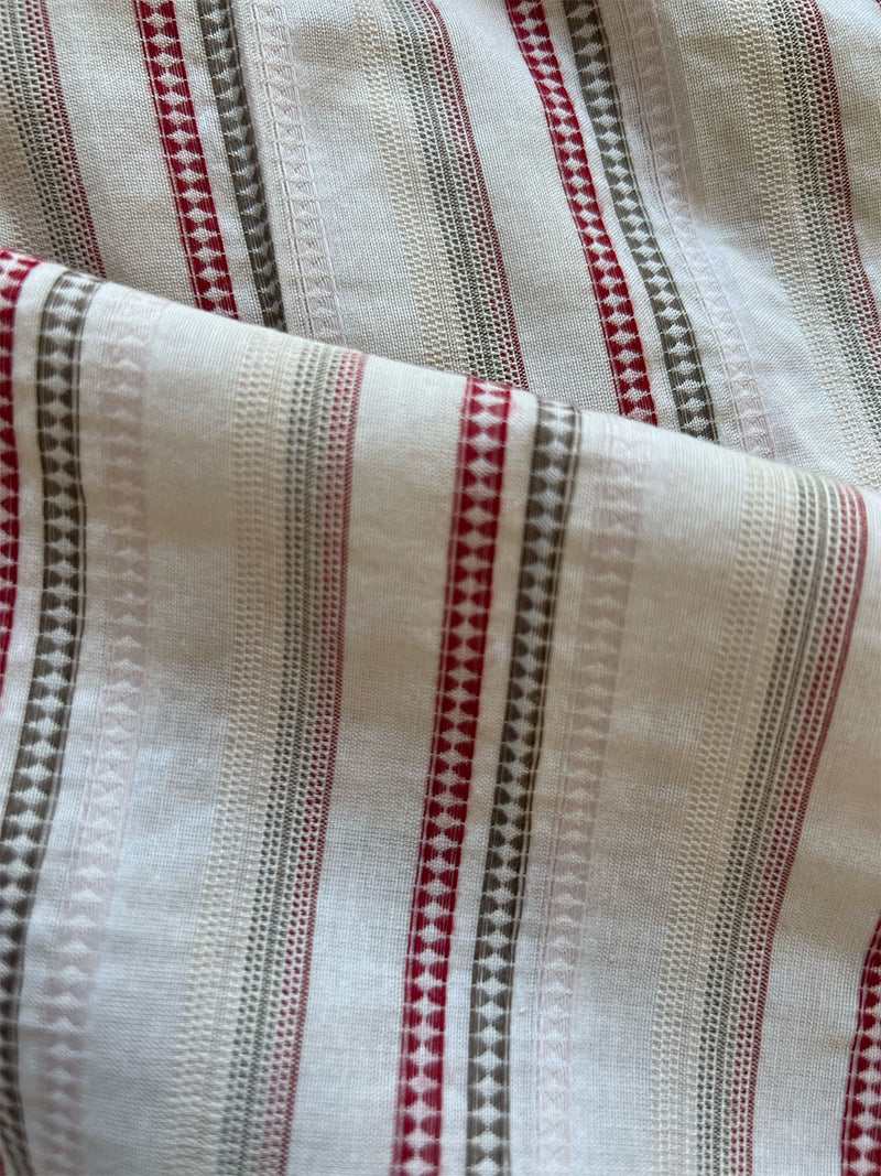 Close up on lemlem imani pink fabric featuring abstract chevron print mixed with shirting-stripe ruffles in soft cream and bright red colors