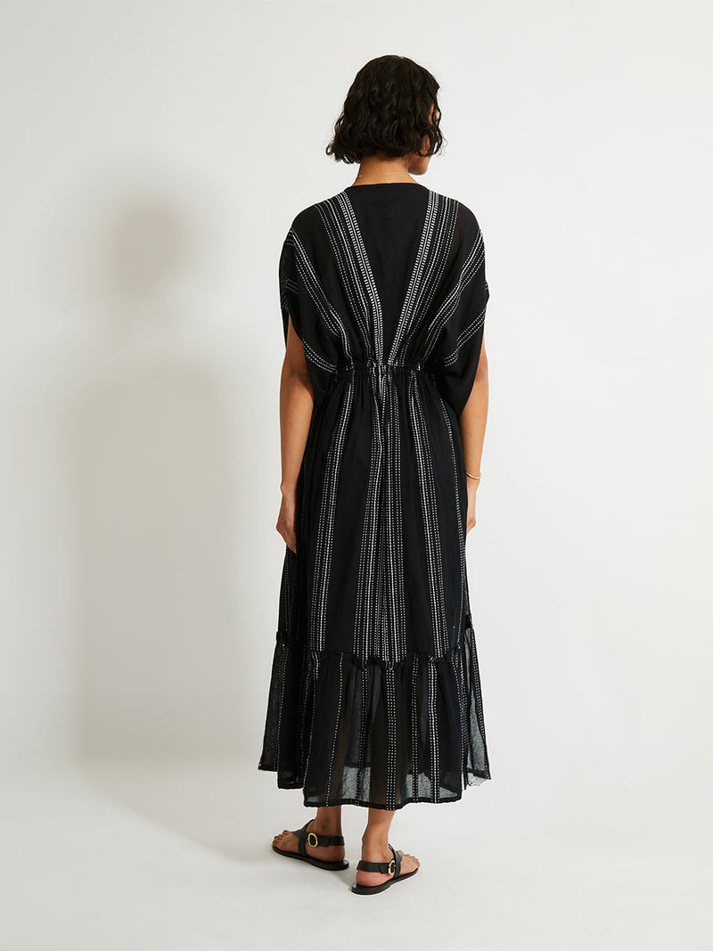 back of a woman woman standing wearing the Leliti Plunge Neck Dress in Black with white stitching allover.