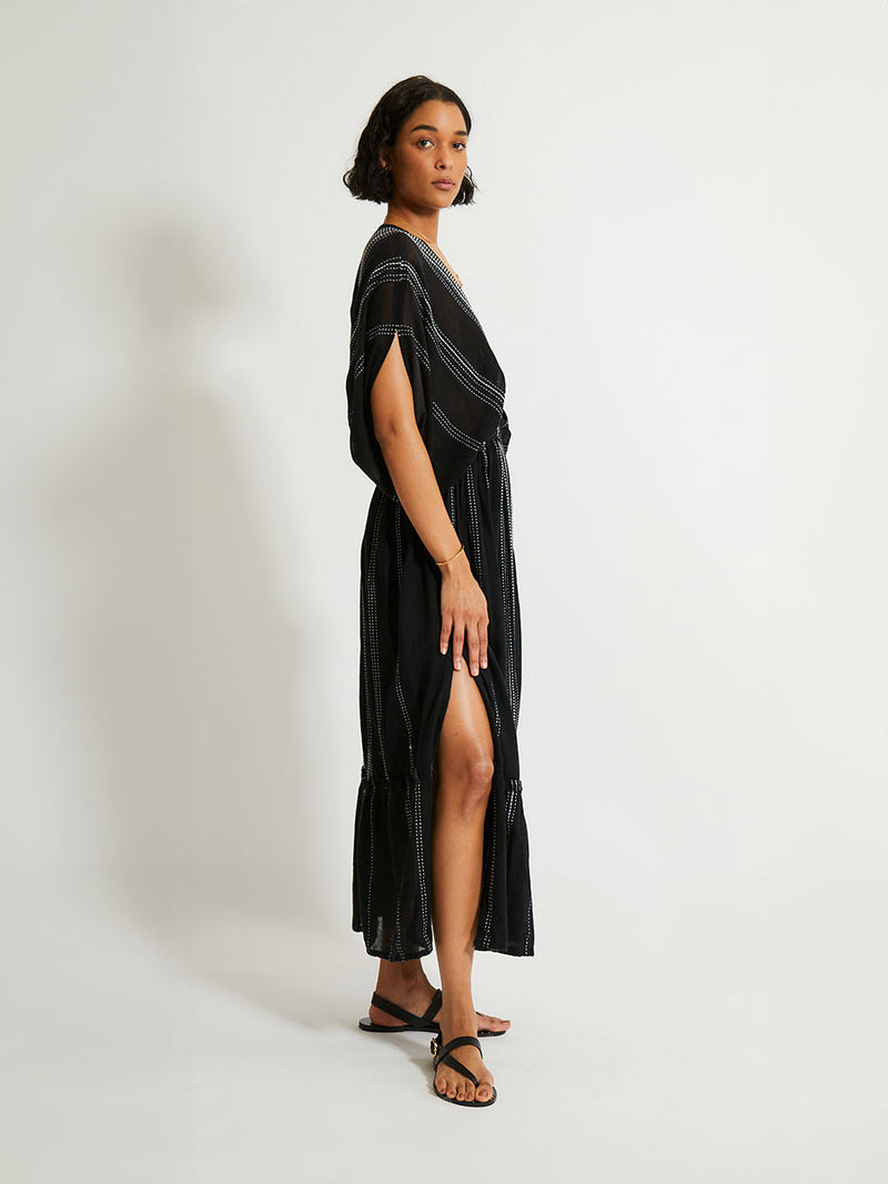 side shot of a woman standing wearing the Leliti Plunge Neck Dress in Black with white stitching allover.