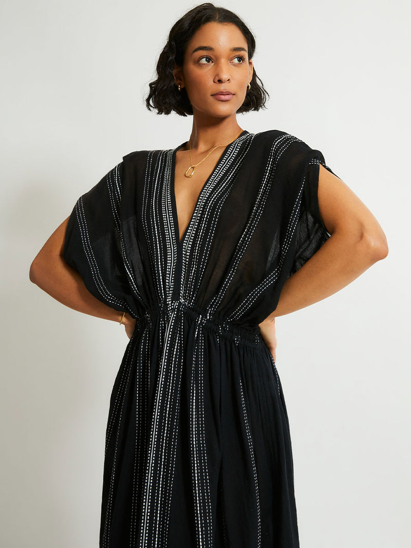 close up on a woman standing wearing the Leliti Plunge Neck Dress in Black with white stitching allover.