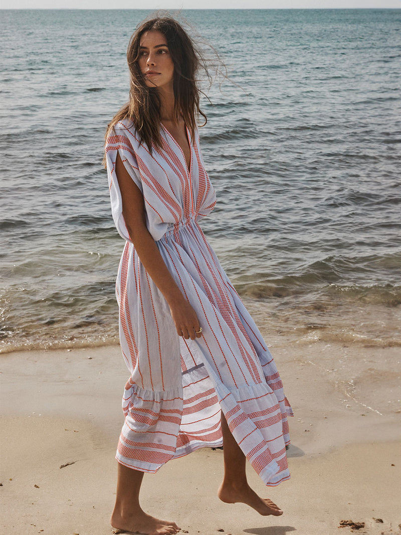 Woman Walking on a beach  Wearing lemlem Plunge Dress featuring playful pattern of red dots becoming stripes on a pale blue background