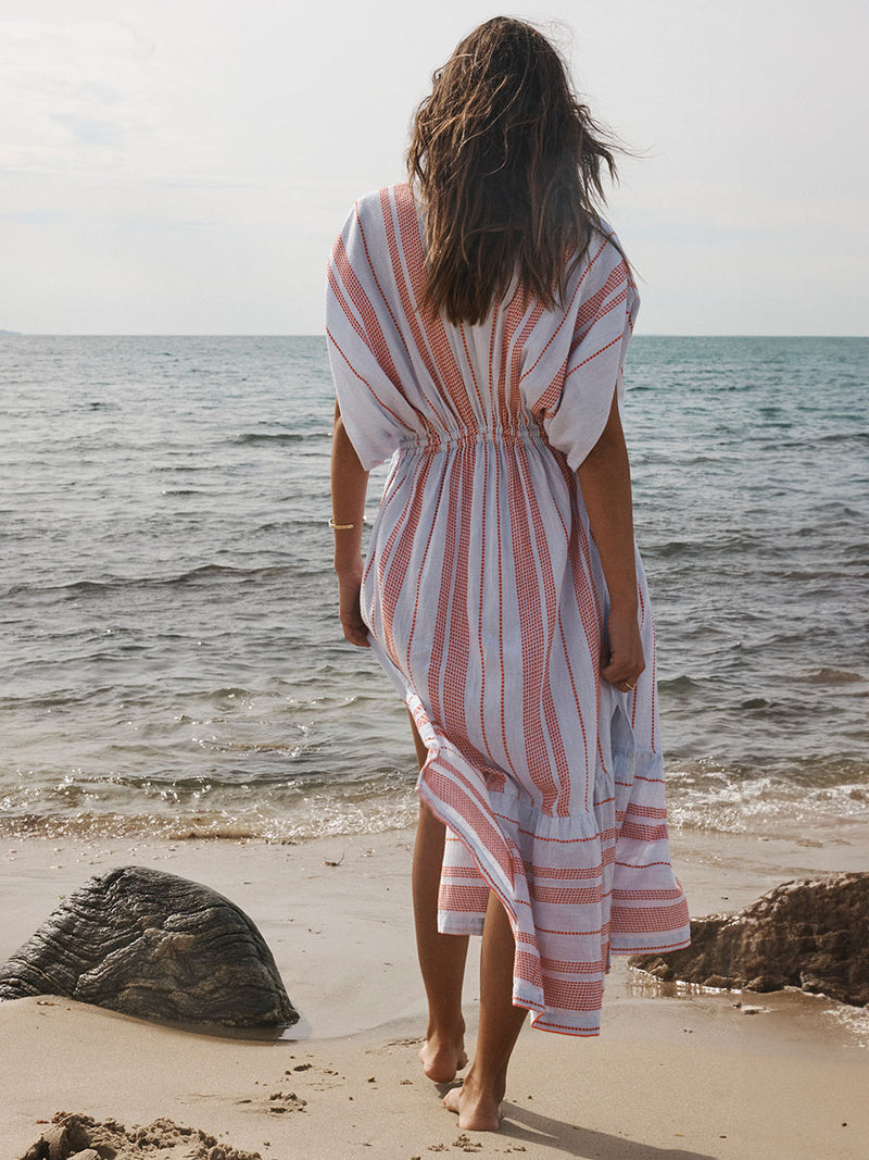 Back of a Woman Walking on a beach Wearing lemlem Plunge Dress featuring playful pattern of red dots becoming stripes on a pale blue background