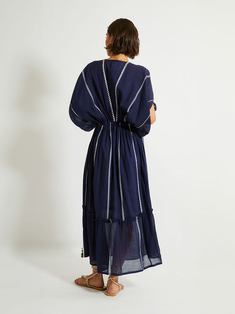 Back view of a woman standing wearing  the Nunu Plunge Neck dress in navy blue featuring a navy with white vertical stripes and graphic lines.