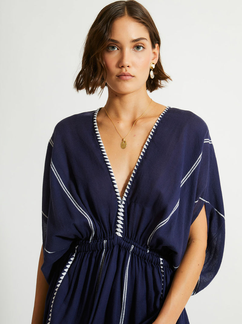 Close up of a Woman standing  wearing  the Nunu Plunge Neck dress in navy blue featuring a navy with white vertical stripes and graphic lines.