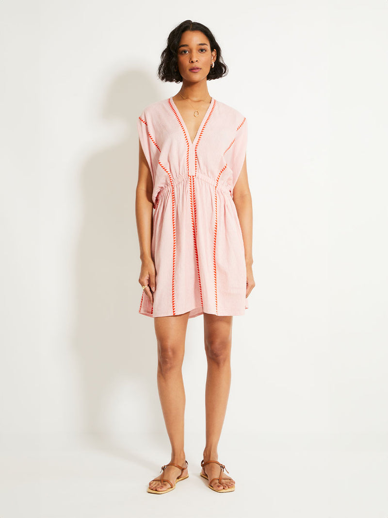 Woman Standing Wearing lemlem ALEM Plunge Dress  featuring vibrant orange red Tibeb pattern on a soft antique rose pink background, with a hint of citron tipping.