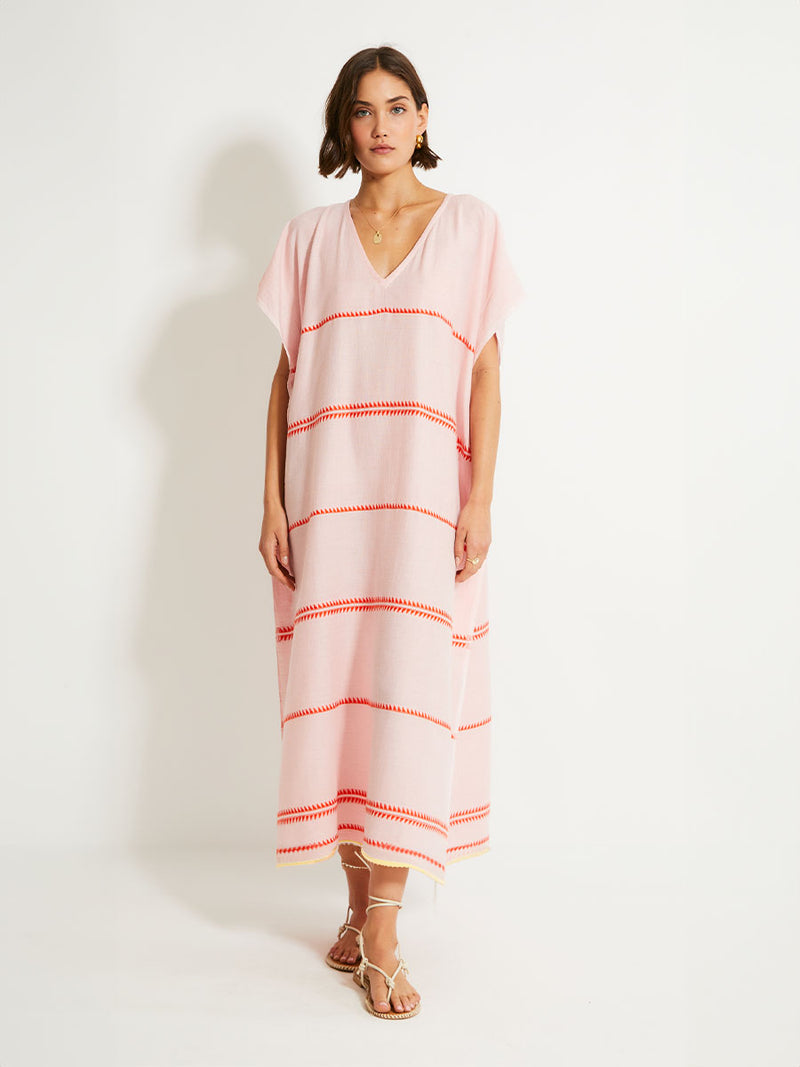 Woman Standing Wearing lemlem DALILA Caftan featuring vibrant orange red Tibeb pattern on a soft antique rose pink background, with a hint of citron tipping.