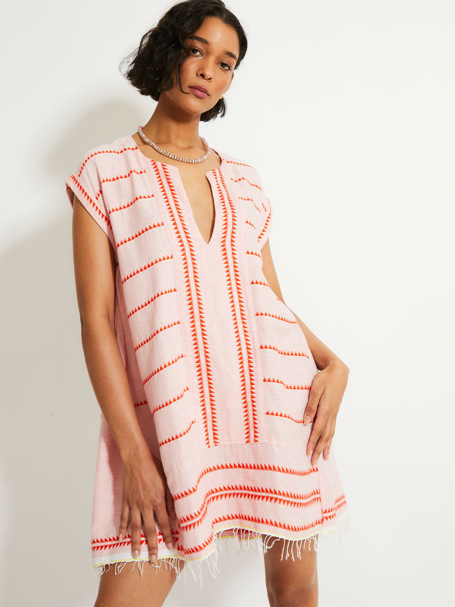 Woman Standing Wearing lemlem ELINA Caftan featuring vibrant orange red Tibeb pattern on a soft antique rose pink background, with a hint of citron tipping.