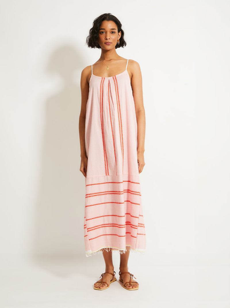 Woman Standing Wearing  lemlem NIA Slip Dress featuring vibrant orange red Tibeb pattern on a soft antique rose pink background, with a hint of citron tipping.