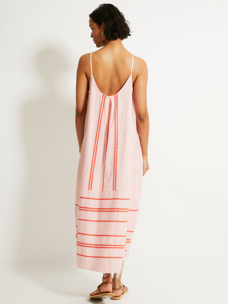 Back of a Woman Standing Wearing  lemlem NIA Slip Dress featuring vibrant orange red Tibeb pattern on a soft antique rose pink background, with a hint of citron tipping.