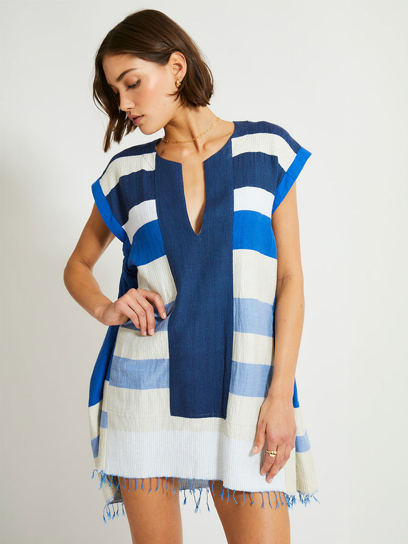 Woman Standing Wearing lemlem Elina Caftan featuring featuring a striking color-block combination of three shades of blue, paired with bands of neutral cream and white