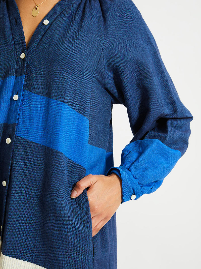 Close up on a Woman Standing Wearing lemlem Makeda Dress featuring a striking color-block combination of three shades of blue, paired with bands of neutral cream and white