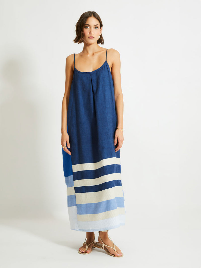 Woman Standing Wearing lemlem NIA Slip Dress featuring a striking color-block combination of three shades of blue, paired with bands of neutral cream and white