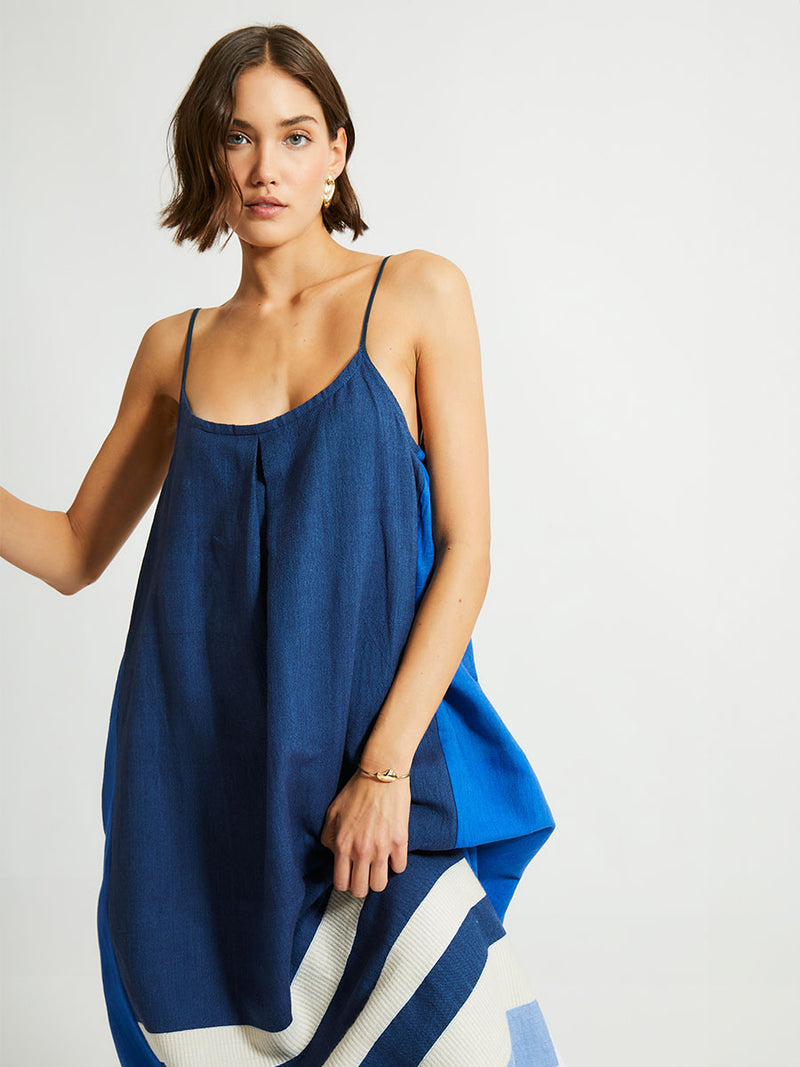 Close up on a Woman Standing Wearing lemlem NIA Slip Dress featuring a striking color-block combination of three shades of blue, paired with bands of neutral cream and white