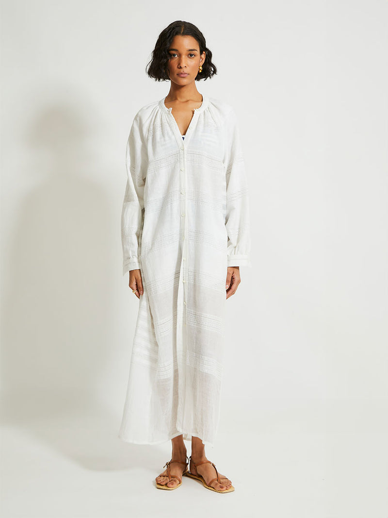 Woman Standing wearing lemlem Makeda Dress featuring  textured solid and sheer weaving highlighted by delicate shimmering silver dots on a bright white background