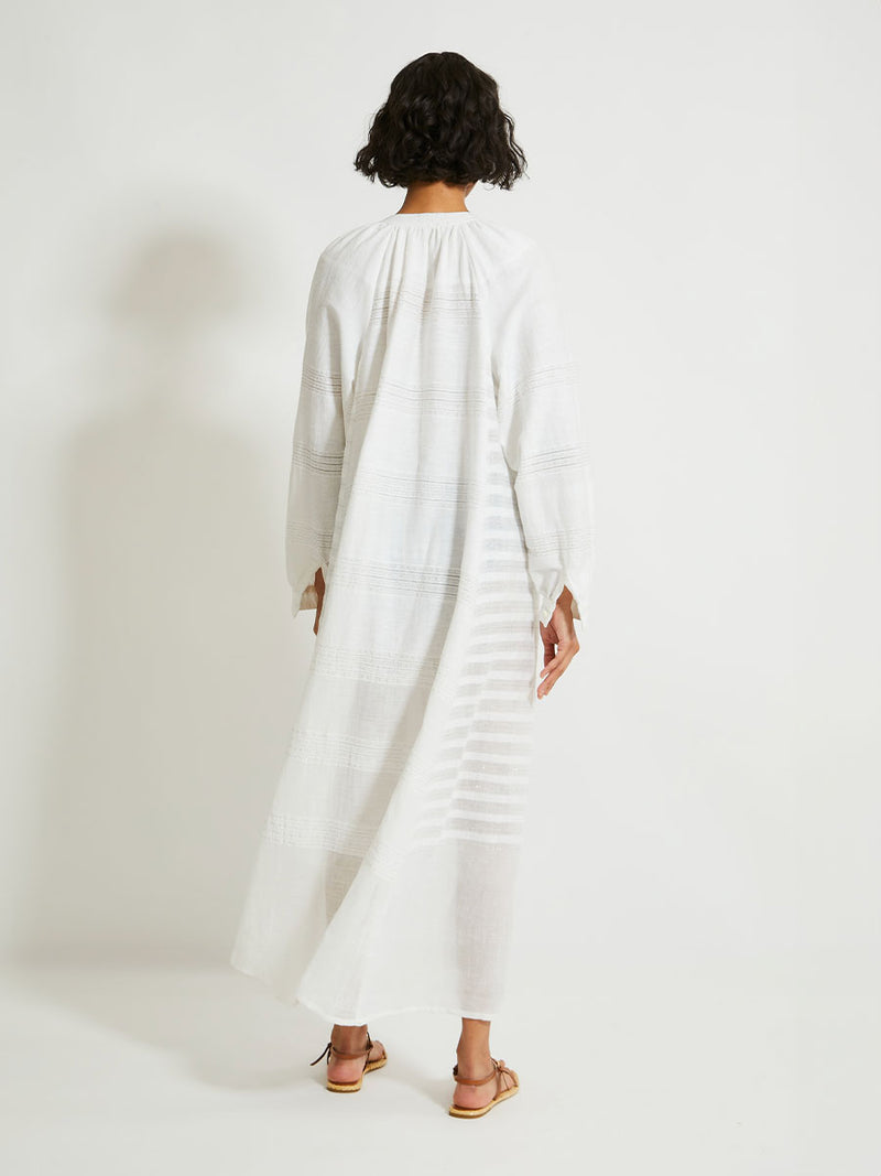 Back of a Woman Standing wearing lemlem Makeda Dress featuring  textured solid and sheer weaving highlighted by delicate shimmering silver dots on a bright white background