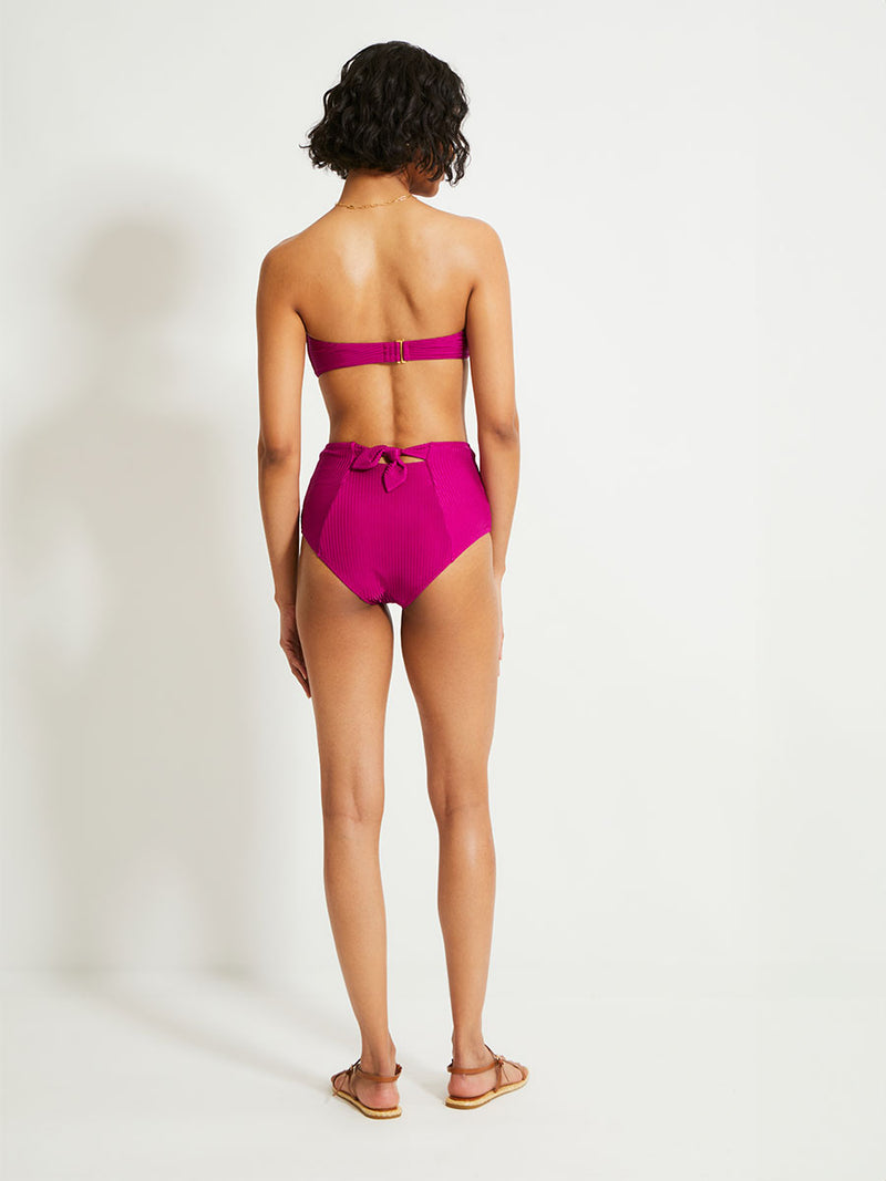 Back of a Woman Standing Wearing lemlem AVA Bandeau Top featuring  rich, opulent berry color and a matching bikini bottom