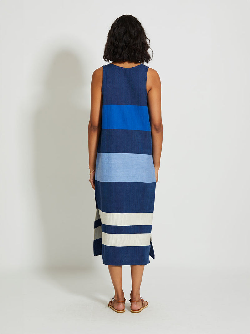 Back of a Woman Standing Wearing lemlem LILIAN Tank Dress featuring a striking color-block combination of three shades of blue, paired with bands of neutral cream and white