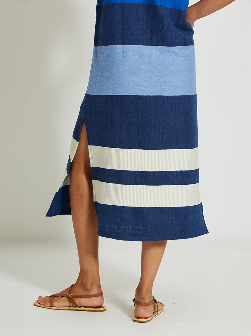 Close up on a  Woman's legs Standing Wearing lemlem LILIAN Tank Dress featuring a striking color-block combination of three shades of blue, paired with bands of neutral cream and white