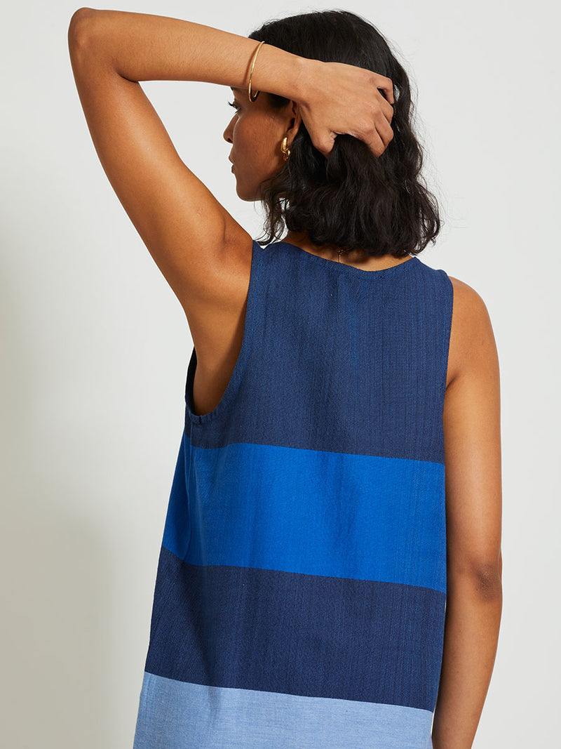 Back of a Woman Standing Wearing lemlem LILIAN Tank Dress featuring a striking color-block combination of three shades of blue, paired with bands of neutral cream and white