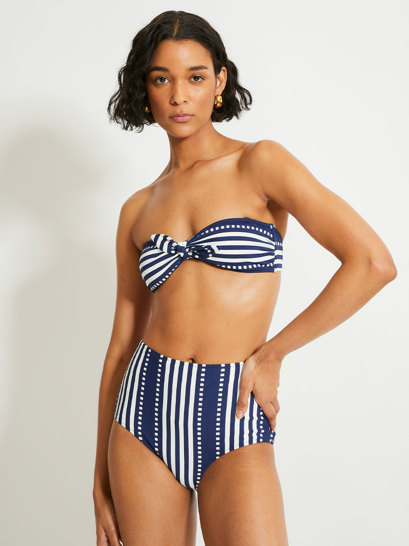 Woman Standing Wearing lemlem Ava Bandeau Top featuring a classic navy background with ivory stripes and dots and matching high waist bottom