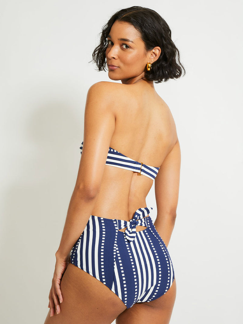 Back of a Woman Standing Wearing lemlem ELSI High Waist Bottom featuring a classic navy background with ivory stripes and dots and matching bandeau top