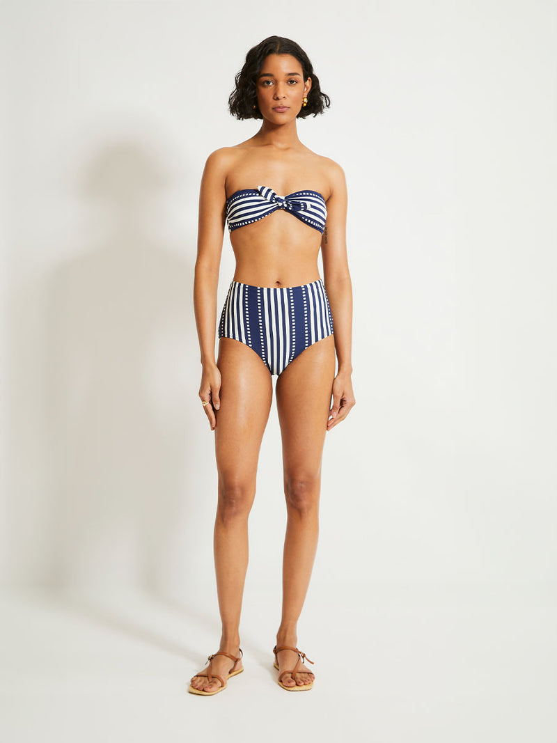 Woman Standing Wearing lemlem Ava Bandeau Top featuring a classic navy background with ivory stripes and dots and matching high waist bottom