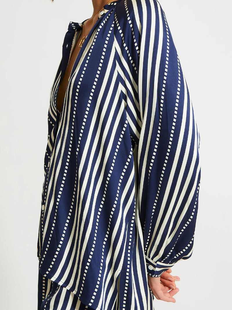 Close up on a Woman Standing Wearing lemlem Mita Blouse featuring a classic navy background with ivory stripes and dots on a silky fabric and matching shorts