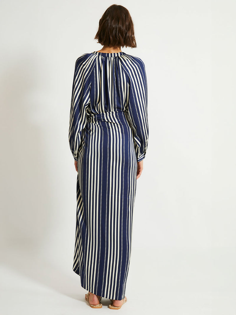 Back of a woman standing wearing lemlem ADIA Sarong featuring a classic navy background with ivory stripes and dots on a silky fabric and a matching blouse