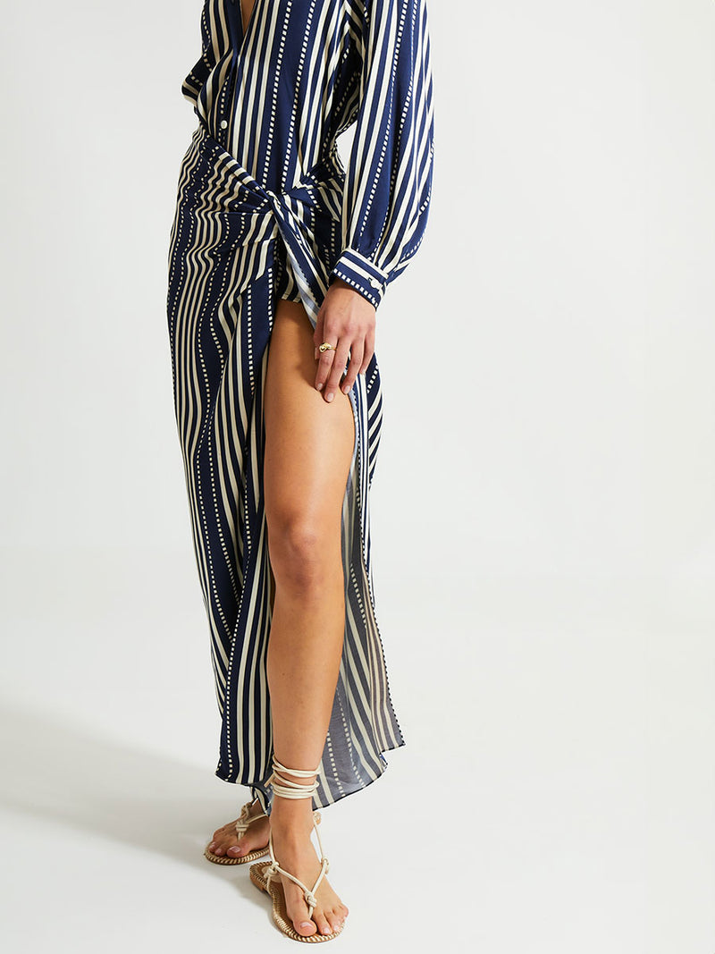 Close up on a woman standing wearing lemlem ADIA Sarong featuring a classic navy background with ivory stripes and dots on a silky fabric and a matching blouse