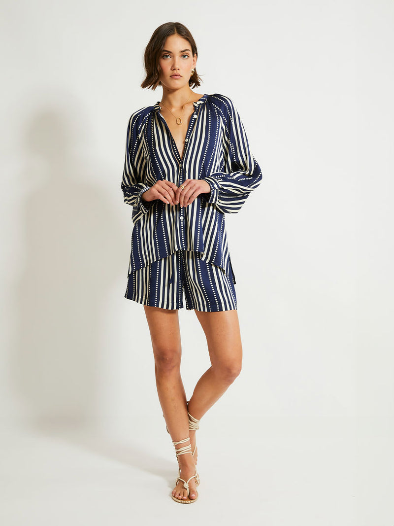 Woman Standing Wearing lemlem Mita Blouse featuring a classic navy background with ivory stripes and dots on a silky fabric and matching shorts