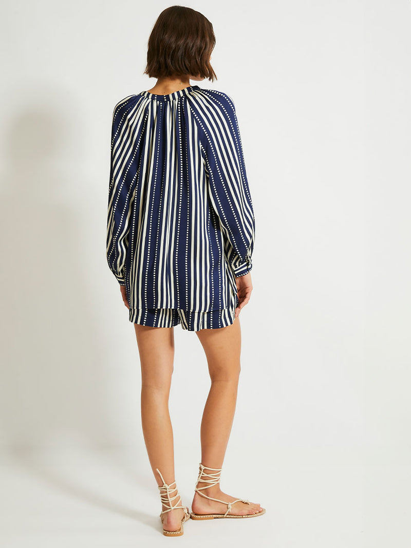 Back of a Woman Standing Wearing lemlem Mita Blouse featuring a classic navy background with ivory stripes and dots on a silky fabric and matching shorts