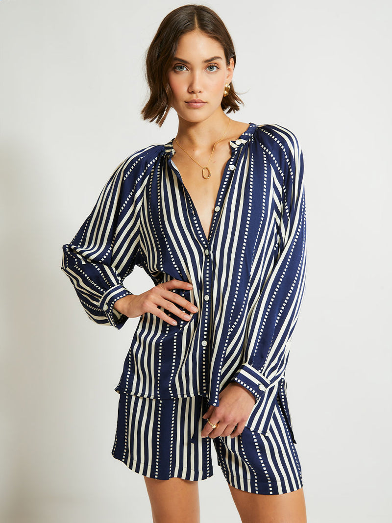 Woman Standing Wearing lemlem Mita Blouse featuring a classic navy background with ivory stripes and dots on a silky fabric and matching shorts