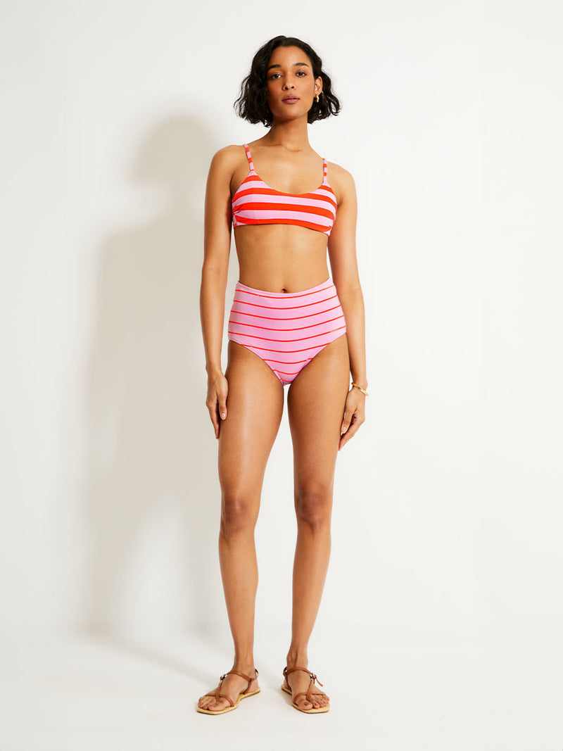 Woman Standing Wearing lemlem ELSI High Waist Bottom featuring soft pink color accented by neon orange red stripes and scoop top